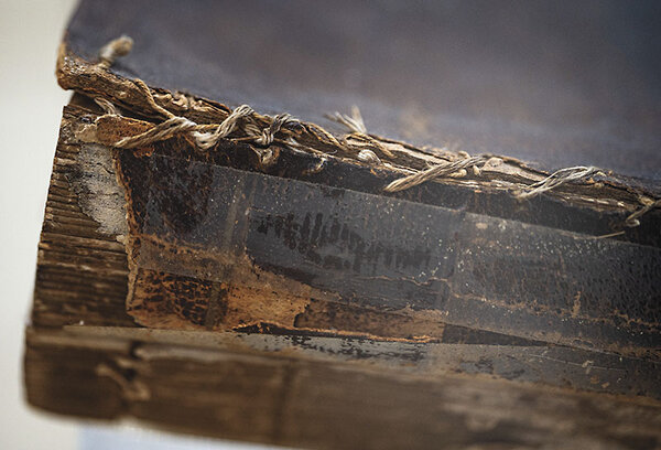 The corner of a Bible with hand sewn binding is cracked and worn.
